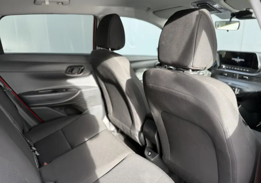 Vue intérieure arrière de la Hyundai i20 rouge Dragon Metal, sièges tissu noirs et tableau de bord avec écran tactile visible.