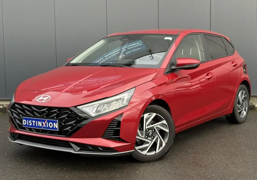 Vue 3/4 avant droite d'une Hyundai i20 2025 rouge Dragon Metal avec jantes alliage diamantées et calandre noire.