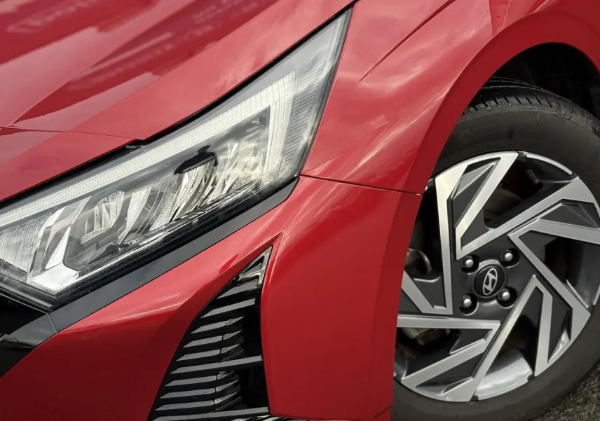 Gros plan sur l'avant droit rouge Dragon Metal d'une Hyundai i20 2025, mettant en valeur le phare LED et la jante alliage diamantée.