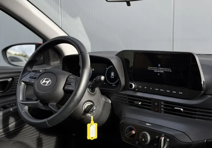 Vue intérieure côté conducteur de la Hyundai i20 2025, volant cuir, tableau de bord numérique et écran tactile central.