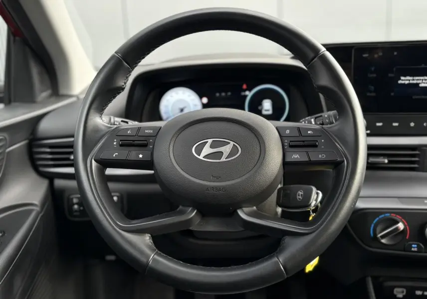 Vue rapprochée du volant cuir multifonction de la Hyundai i20 2025 avec tableau de bord numérique et commandes intégrées.