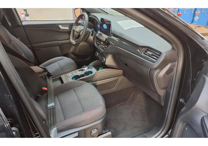 Vue intérieure côté conducteur du Ford Kuga noir Agathe 2024, mettant en valeur les sièges tissu avec surpiqûres rouges et la console centrale moderne.