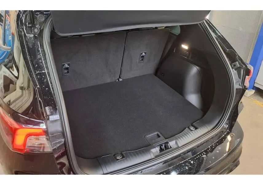 Coffre ouvert vu de l'arrière droit du Ford Kuga noir Agathe 2024 avec plancher de coffre plat et éclairage intérieur.