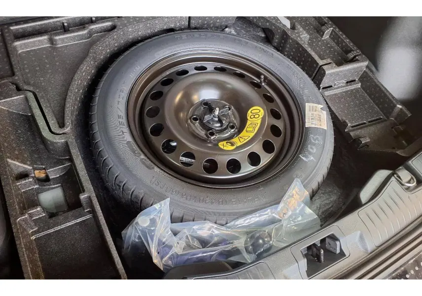 Roue de secours galette noire dans le coffre d'un Ford Kuga 2024, avec compartiments de rangement en mousse noire.