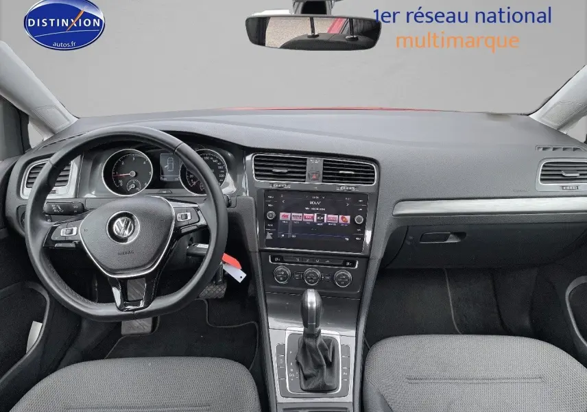 Vue intérieure frontale du tableau de bord et volant noir d'une Volkswagen Golf VII rouge, avec écran tactile central et boîte automatique.