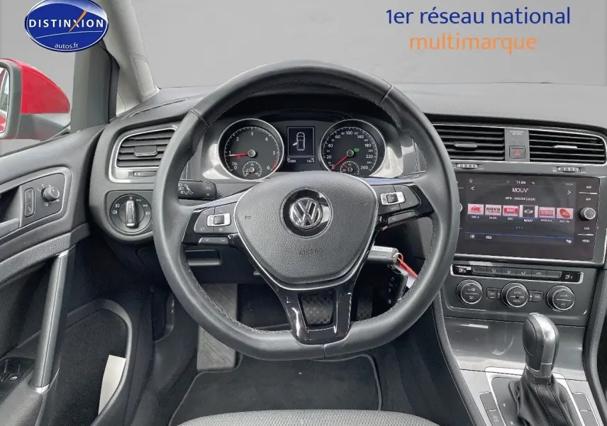 Vue intérieure centrée sur le volant et le tableau de bord d’une Volkswagen Golf rouge, avec écran tactile et commandes visibles.