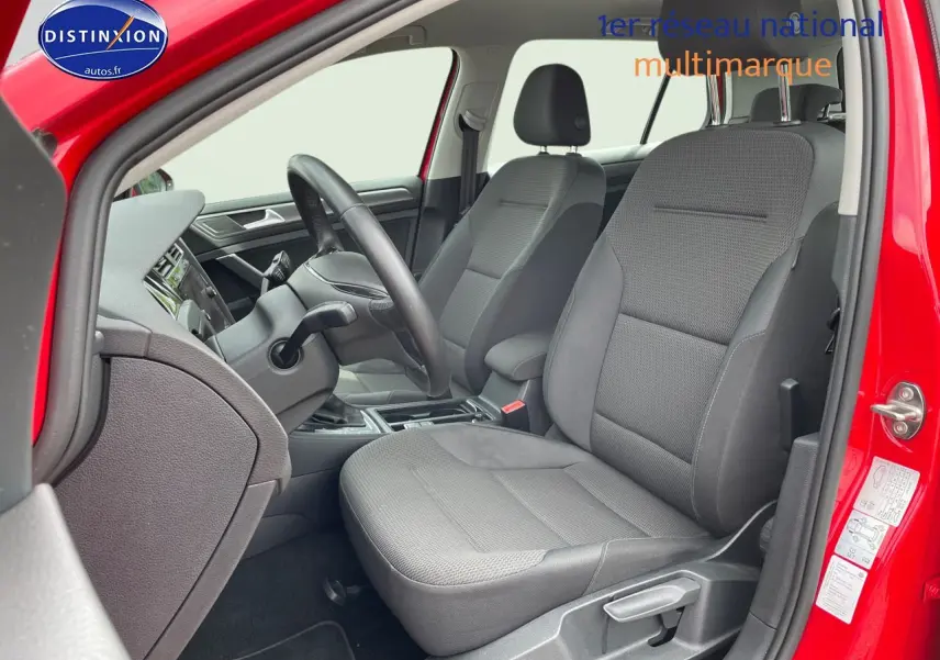 Vue intérieure côté conducteur d’une Volkswagen Golf rouge de 2018, sièges tissu gris et tableau de bord noir.