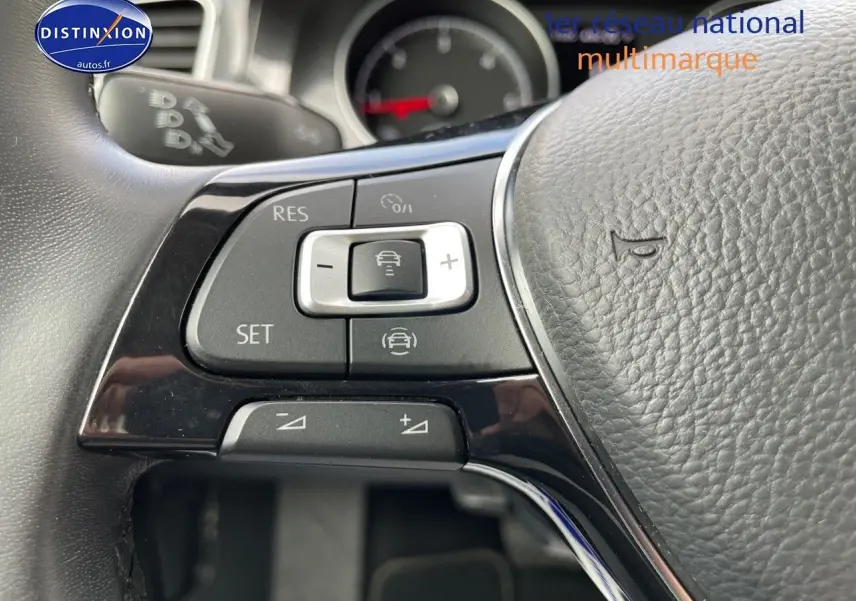 Gros plan sur le volant noir de la Volkswagen Golf VII avec commandes de régulateur de vitesse visibles.