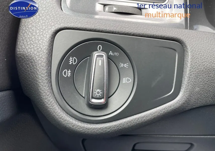 Gros plan sur le bouton de commande des phares dans l’habitacle noir d’une Volkswagen Golf VII rouge.