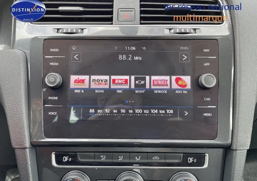 Vue rapprochée de la console centrale de la Volkswagen Golf VII rouge, mettant en valeur l’écran tactile multimédia et les commandes de climatisation.