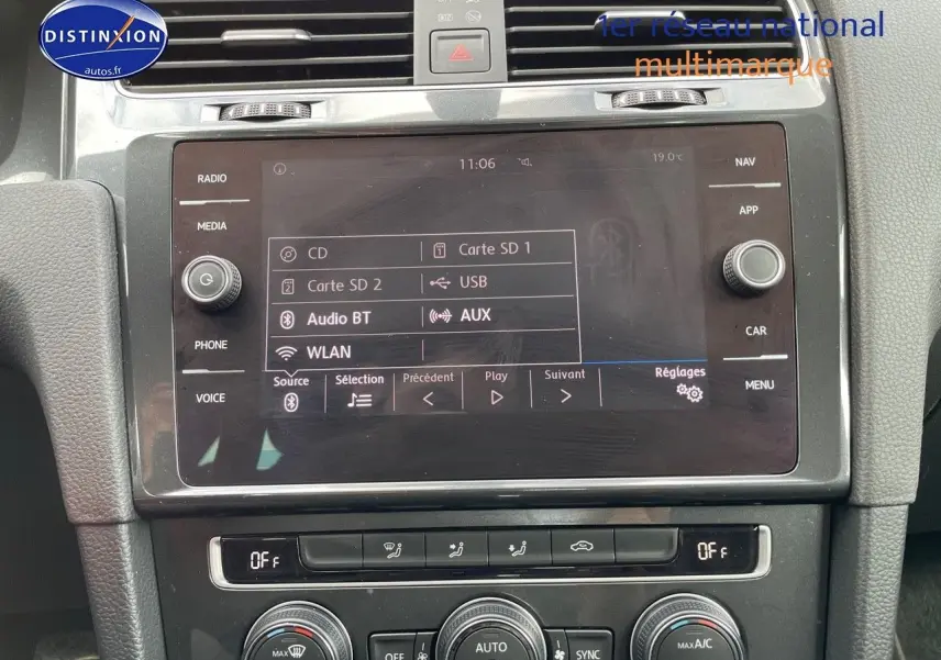 Vue rapprochée de l’écran multimédia et des commandes de climatisation d’une Volkswagen Golf VII rouge, intérieur noir.