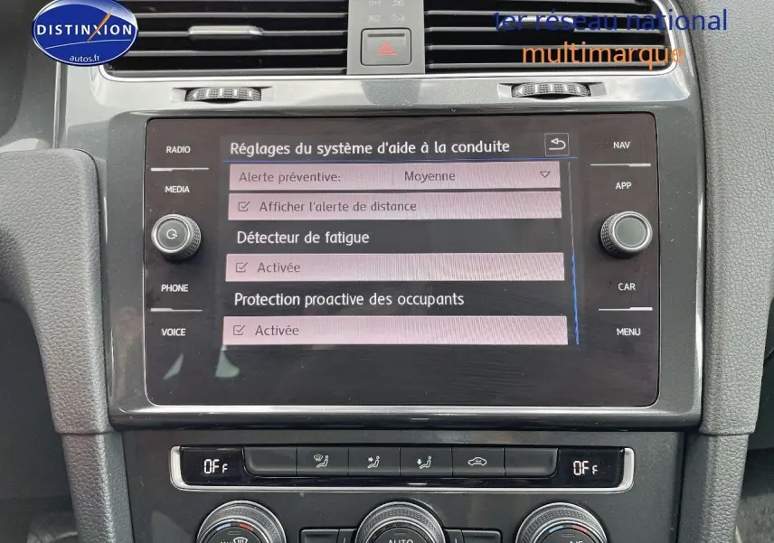 Vue rapprochée de l’écran central tactile et de la console de la Volkswagen Golf rouge, affichant les réglages d’aide à la conduite.