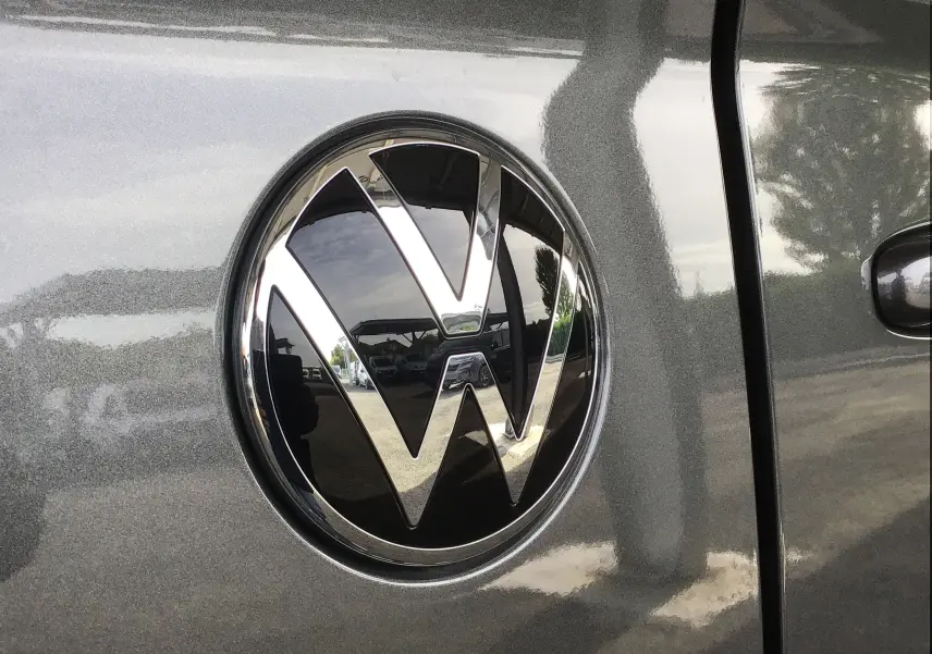 Gros plan sur l'emblème Volkswagen chromé sur la porte gris anthracite du Transporter T7 L2H1 2025.