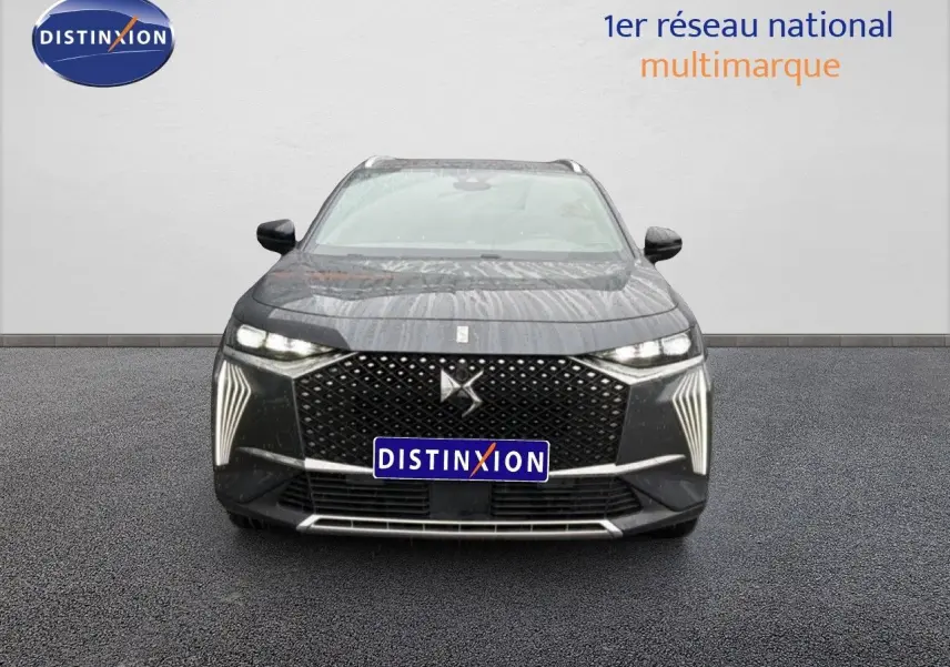 Vue de face du DS7 gris titane métal avec sa calandre distinctive et ses feux LED verticaux allumés.