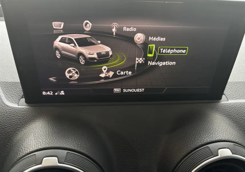 Écran central affichant le menu multimédia avec une Audi Q2 grise vue de 3/4 avant sur l'interface.