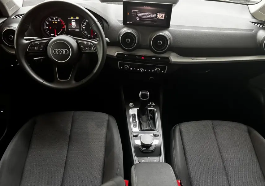 Vue intérieure de l'Audi Q2 35 TFSI S Line 2023, tableau de bord noir avec volant cuir et console centrale moderne.