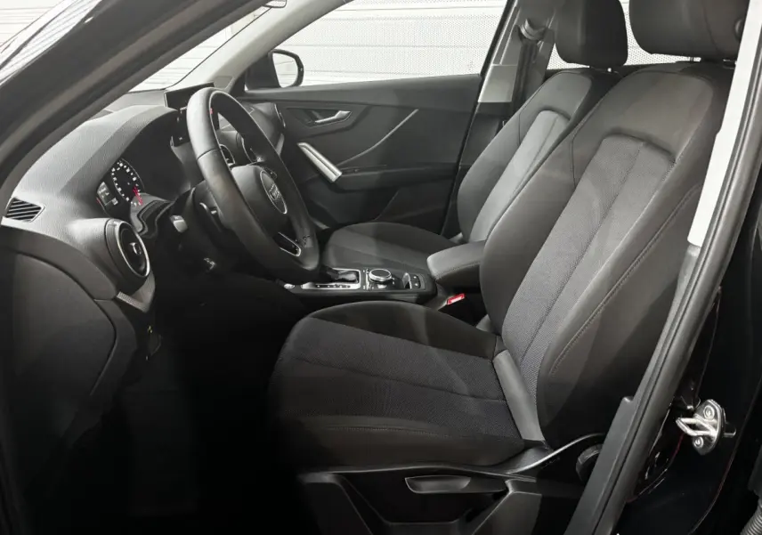 Vue intérieure côté conducteur de l'Audi Q2 noir 2023, mettant en valeur les sièges avant et le volant cuir multifonctions.