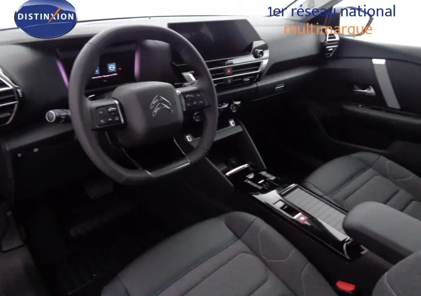Vue intérieure côté conducteur de la Citroën C4 2023, tableau de bord noir avec volant multifonction et sièges tissu noir.