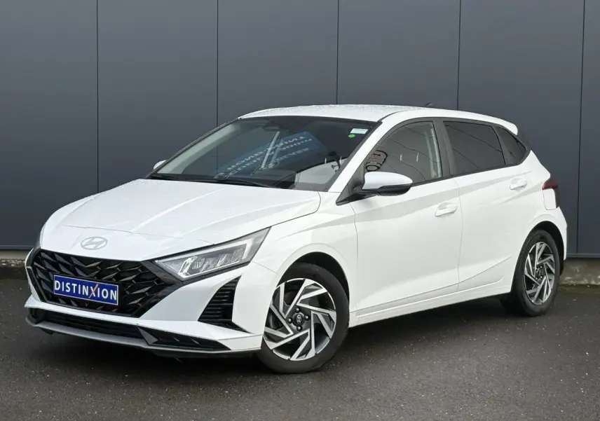 Vue 3/4 avant gauche d'une Hyundai i20 blanche Atlas avec jantes alliage diamantées et calandre noire distinctive.