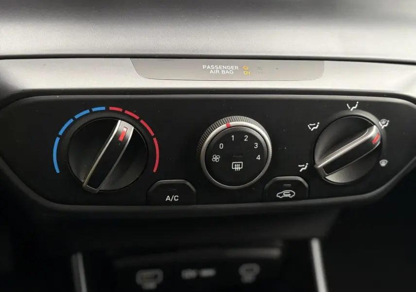 Vue rapprochée du tableau de bord noir de la Hyundai i20 2025 montrant les commandes manuelles de climatisation.