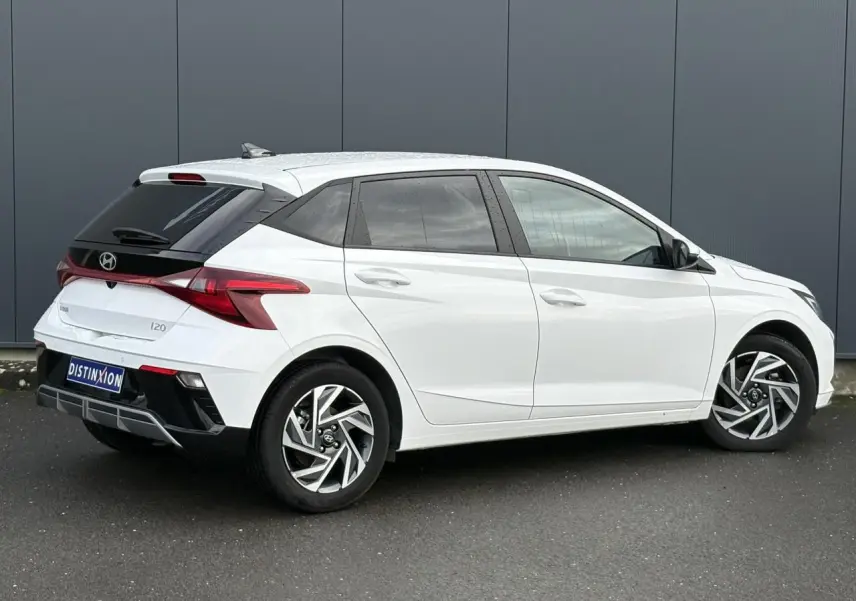 Vue 3/4 arrière droite d'une Hyundai i20 blanche Atlas avec jantes alliage 16'' diamantées et vitres surteintées.