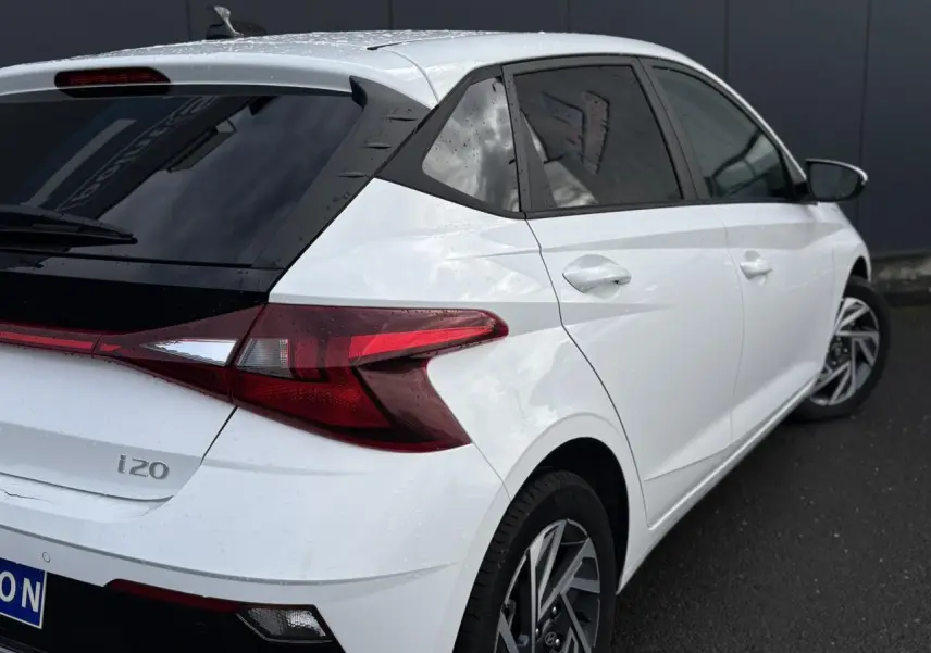 Vue 3/4 arrière droite d'une Hyundai i20 blanche Atlas avec jantes alliage 16'' diamantées et vitres surteintées.