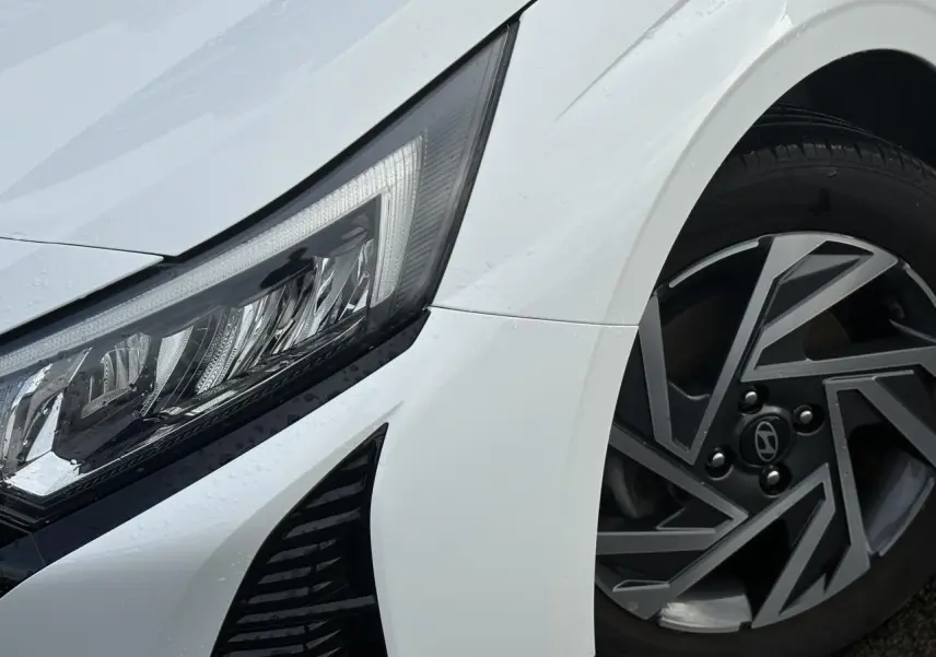 Gros plan sur l'avant droit blanc Atlas de la Hyundai i20 2025, mettant en valeur le phare LED et la jante alliage diamantée.