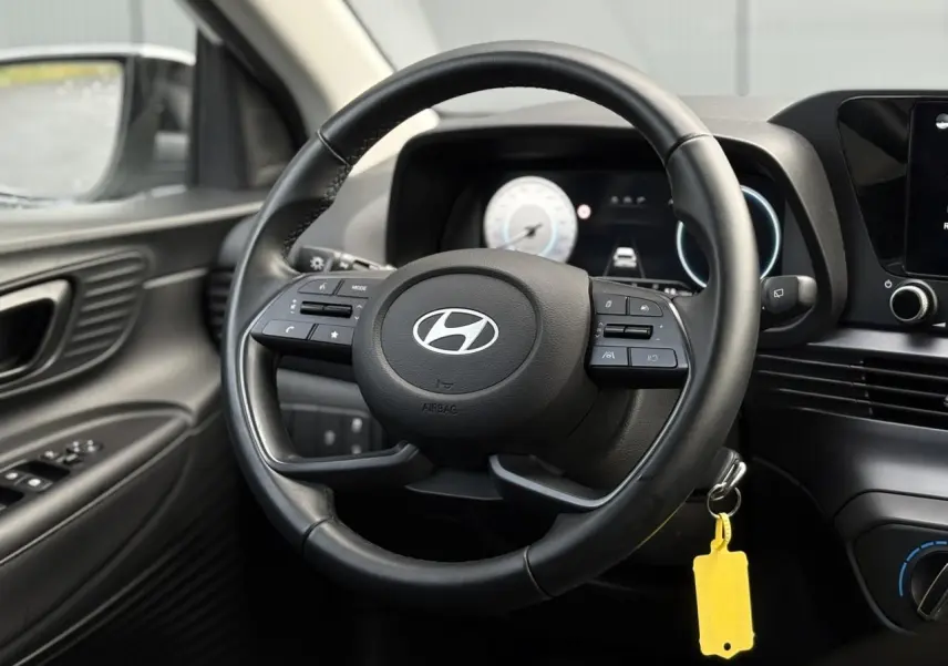 Vue intérieure centrée sur le volant cuir noir de la Hyundai i20 2025 avec tableau de bord numérique et commandes intégrées.