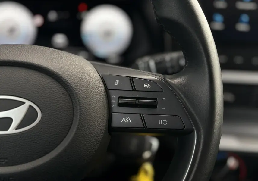 Gros plan sur le volant cuir noir de la Hyundai i20 2025, avec commandes de régulateur de vitesse et assistance au maintien de voie.