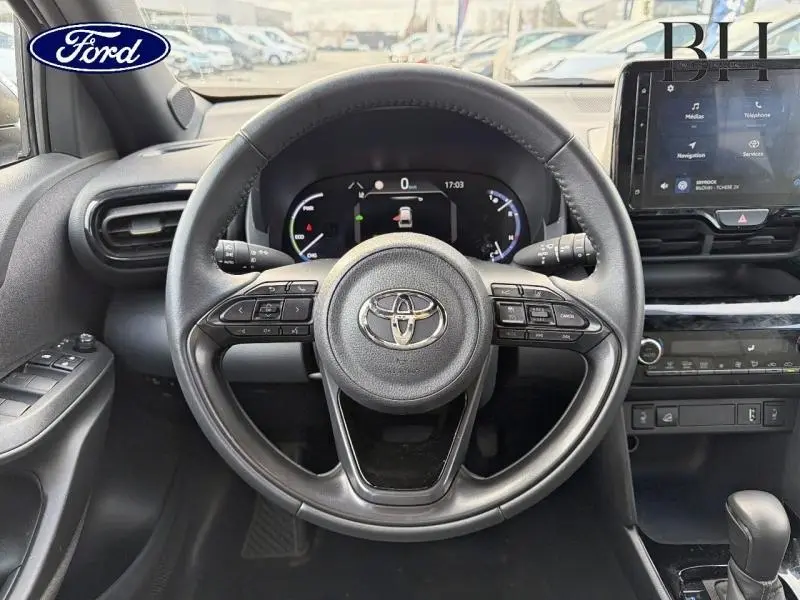 Vue intérieure centrée sur le volant cuir multifonction d'une Toyota Yaris Cross blanche, avec tableau de bord numérique et écran tactile.