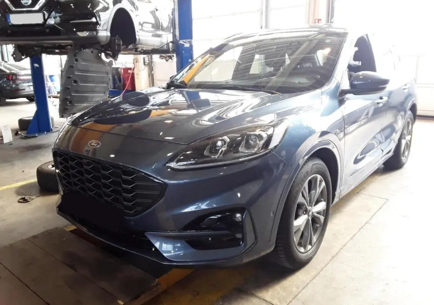 Ford Kuga 2024 bleu azur en 3/4 avant droit, avec calandre noire et jantes alliage visibles en atelier.