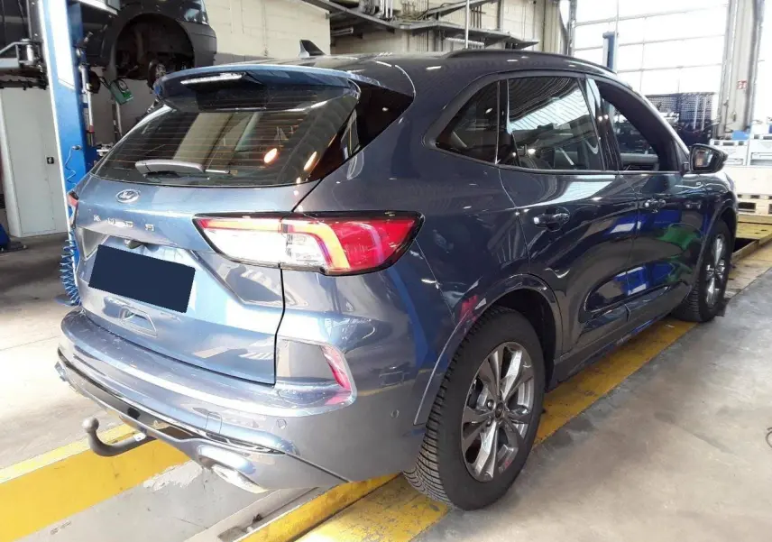 Vue 3/4 arrière droite du Ford Kuga bleu azur 2024 avec crochet d'attelage et jantes alliage 18 pouces en atelier.
