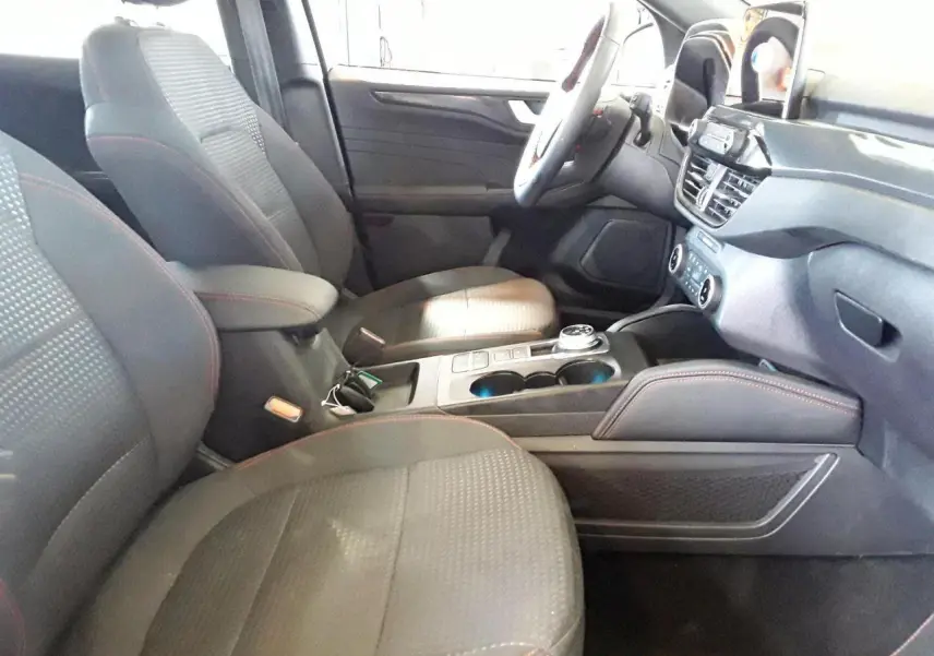 Vue intérieure côté conducteur du Ford Kuga 2024, sièges gris avec surpiqûres rouges et console centrale moderne.