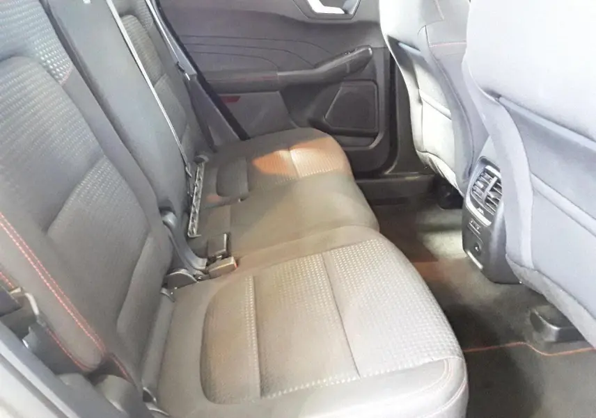 Vue intérieure arrière côté gauche du Ford Kuga 2024, sièges tissu gris avec surpiqûres rouges et aérateurs centraux.