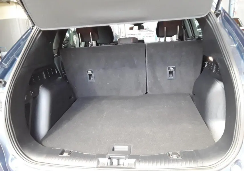 Coffre ouvert vu de l'arrière d'un Ford Kuga bleu azur 2024, montrant l'espace de chargement et les dossiers arrière rabattus.