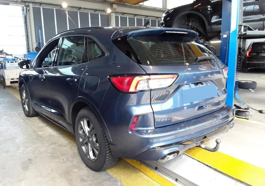 Vue 3/4 arrière droite d’un Ford Kuga bleu azur 2024 avec crochet d’attelage et jantes alliage 18 pouces en atelier.