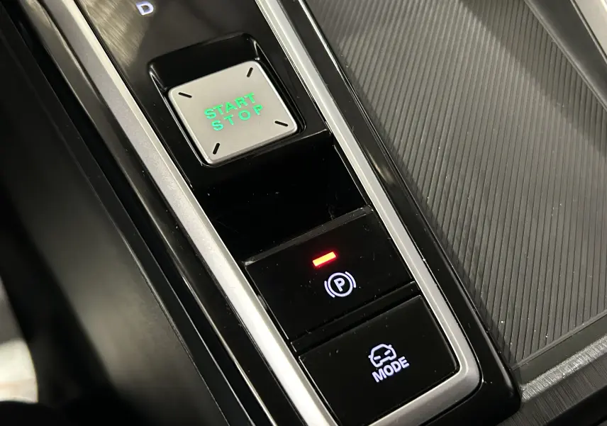 Gros plan sur la console centrale du MG ZS Hybrid+ 2025, avec bouton Start/Stop vert et commandes électroniques noires.