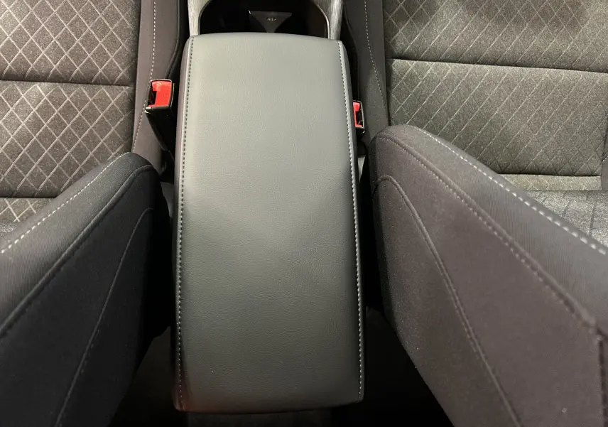 Vue plongeante sur l'accoudoir central noir entre les sièges avant en tissu gris à motifs du MG ZS Hybrid+ 2025.