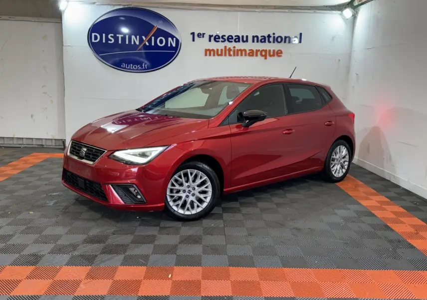 SEAT Ibiza 1.0 TSI 110 FR rouge vue 3/4 avant droit dans un showroom avec sol gris et bandes orange.