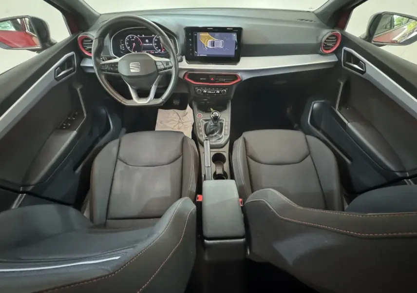 Vue intérieure avant de la SEAT Ibiza 1.0 TSI 110 FR 2024, tableau de bord noir avec touches rouges et écran tactile central.