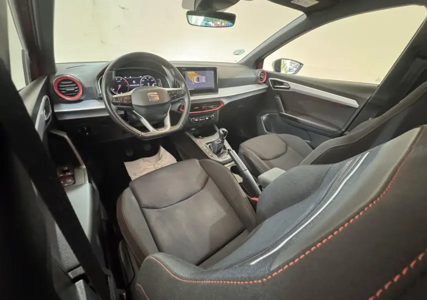 Intérieur de la SEAT Ibiza 1.0 TSI 110 FR 2024 vu côté passager, volant cuir, touches rouges et écran tactile central.