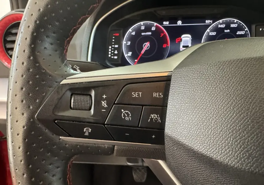 Gros plan sur le volant cuir perforé côté gauche de la SEAT Ibiza 1.0 TSI 110 FR rouge avec commandes multifonctions.