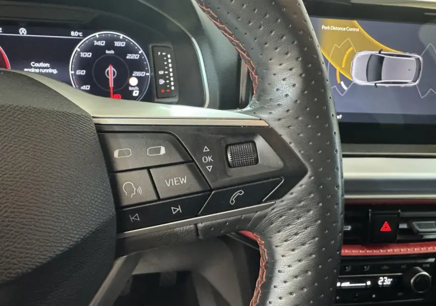 Gros plan sur le volant cuir noir avec surpiqûres rouges du SEAT Ibiza 1.0 TSI 110 FR, affichage numérique et écran tactile.