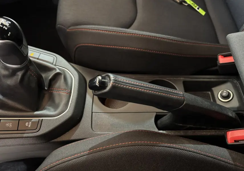 Gros plan sur la console centrale noire de la SEAT Ibiza 2024, frein à main et levier de vitesse avec surpiqûres rouges.