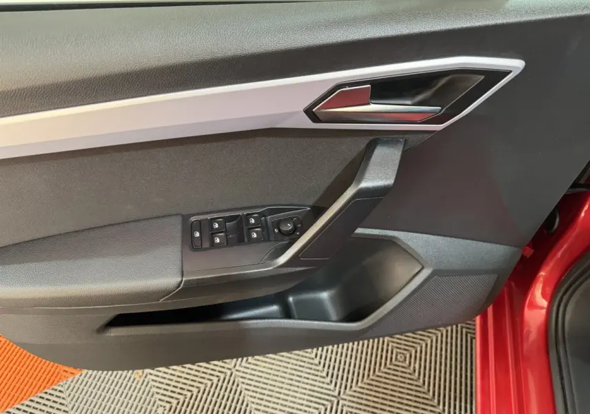 Détail de la porte côté conducteur de la SEAT Ibiza rouge 2024 avec commandes électriques et poignée argentée.