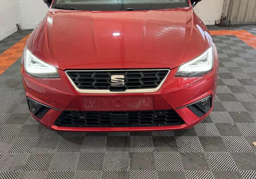 Vue avant rapprochée d'une SEAT Ibiza rouge 2024 avec phares LED allumés et calandre hexagonale noire.