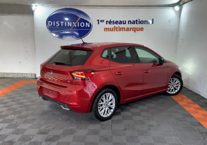 Vue 3/4 arrière droite d'une SEAT Ibiza 1.0 TSI 110 FR rouge avec jantes alliage et feux LED allumés.