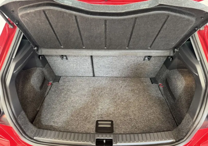 Coffre ouvert de la SEAT Ibiza 1.0 TSI 110 FR rouge, montrant l’espace de rangement et la moquette grise.