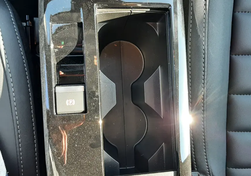 Vue plongeante sur la console centrale noire brillante de la Citroën C4 blanche, avec porte-gobelets et frein à main électrique.