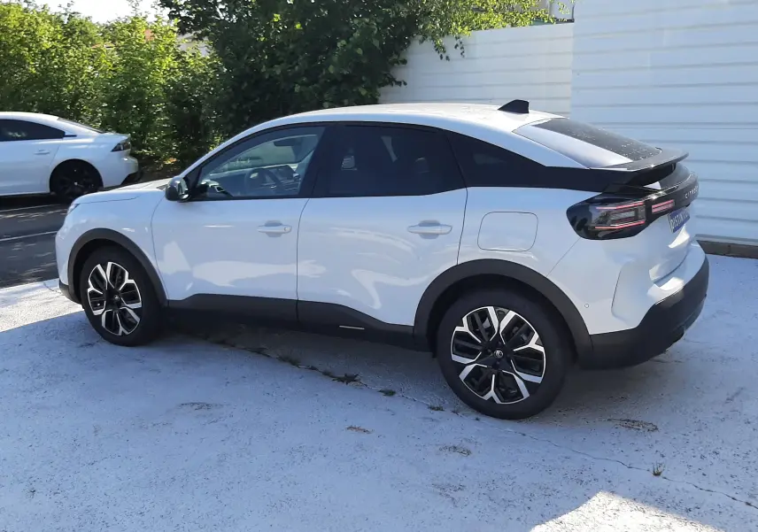 Vue 3/4 arrière droite d'une Citroën C4 blanche Okenite avec toit noir et jantes bi-ton, stationnée en extérieur.